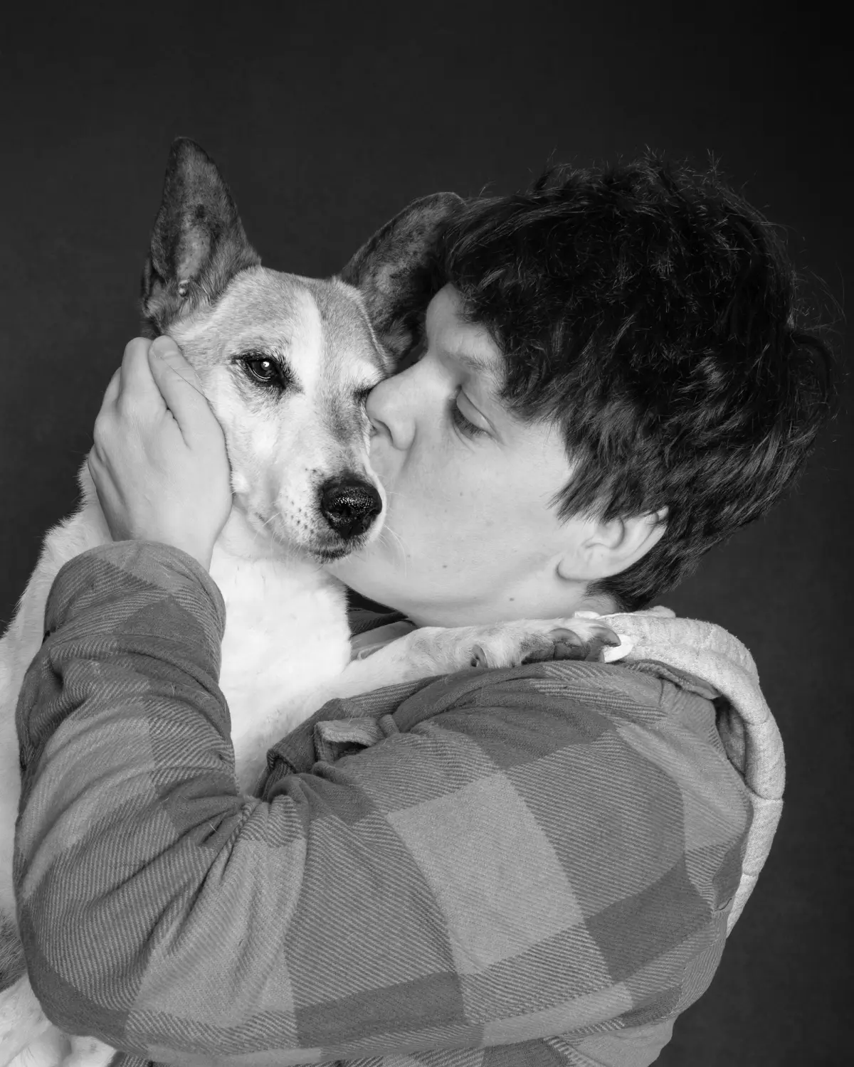 Black and white photo of a person kissing their small white dog