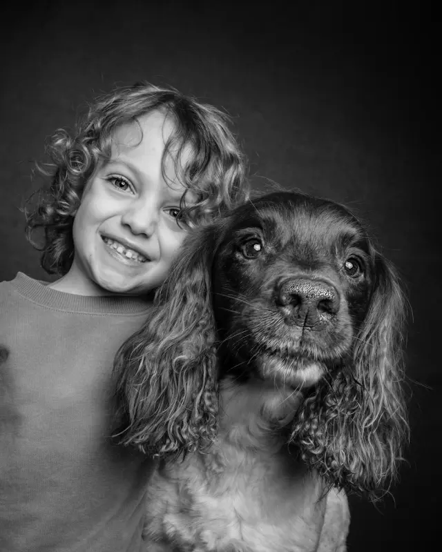 Smiling child cuddling their spaniel, in black and white